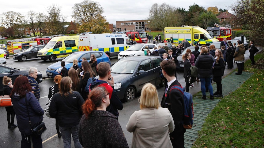 Pupils and staff stand outside the school as emergency services attend to the fainting incident.