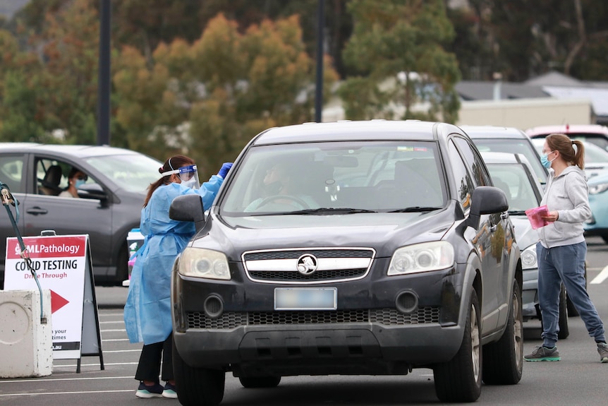 A person in PPE reaches into a car to test a driver for COVID-19.
