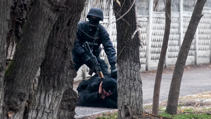 An armed riot police officer holds a gun to the back of a protester on the ground.