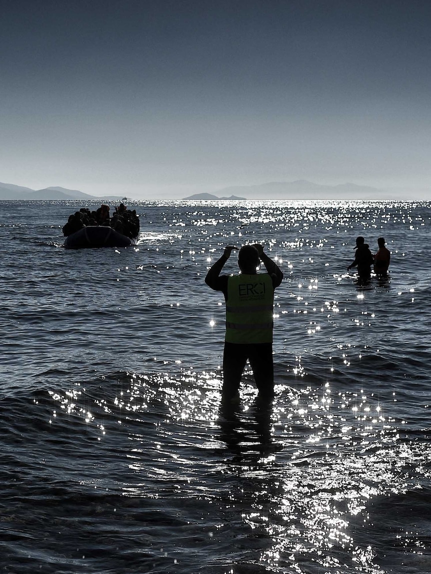 Members of the non-profit organisation Emergency Response Centre International (ERCI) gesture from the shore to a boat carrying refugees and migrants as it arrives in Greece