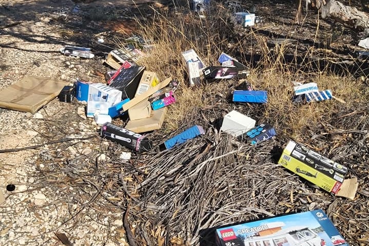 Cardboard boxed and plastic packaging are spread all over the ground, in between trees and bushes.