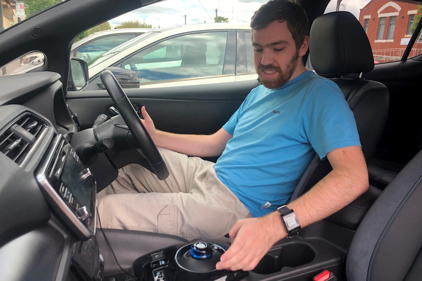 A man in a blue shirt sits in the driver's seat of a black car.