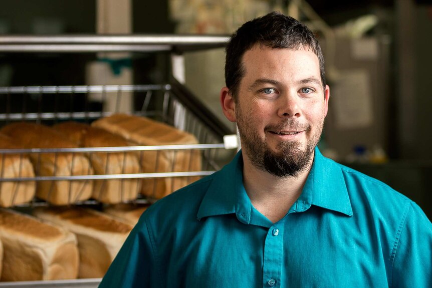 Man stands in front of racks of bread loaves