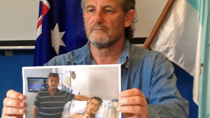 Peter Mitchell holds a picture of his son Matthew in hospital
