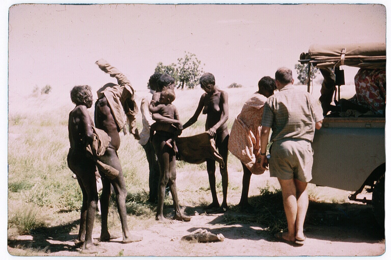 Una foto antigua muestra a personas paradas junto a una camioneta, algunas desnudas, otras atractivas.