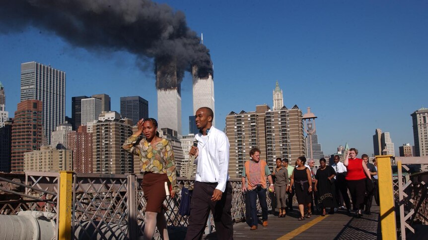 People walk over the Brooklyn Bridge as the World Trade Centre towers burn behind them