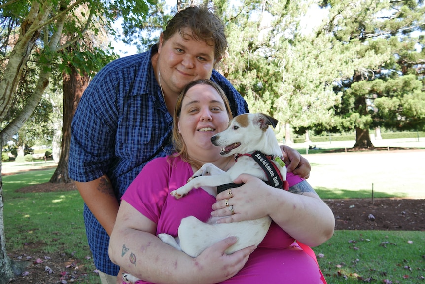 A man in a blue shirt and a woman in a pink shirt hold up a jack russell dog