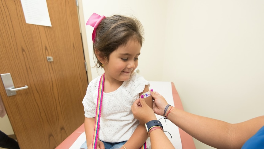 A child looks down at the bandaid a nurse has put on her arm after vaccination.