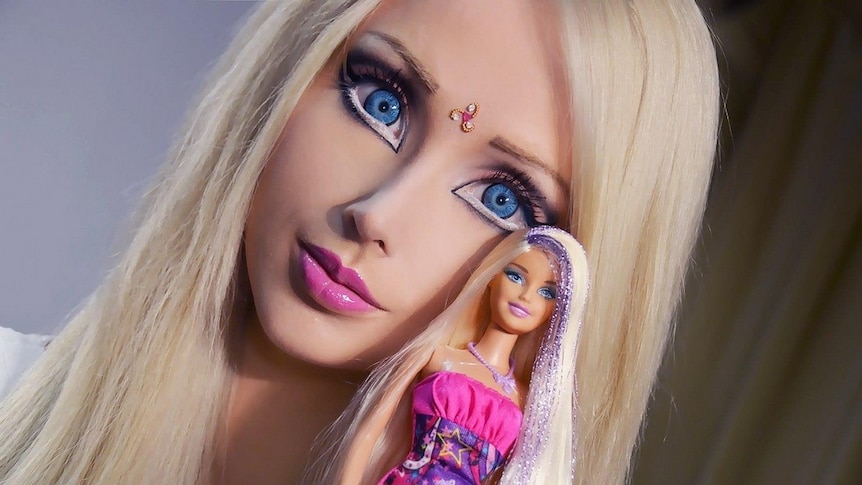 A woman who looks like Barbie, holding a Barbie doll