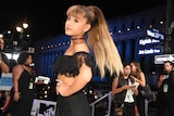 Ariana Grande faces the camera with her hand on her hips.