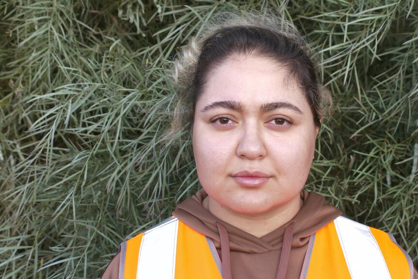 A women wearing orange high vis and standing in front of a bushs