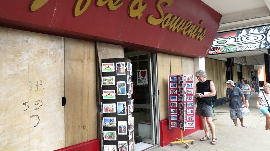 Tourists look at postcards outside a boarded-up shop in Port Vila