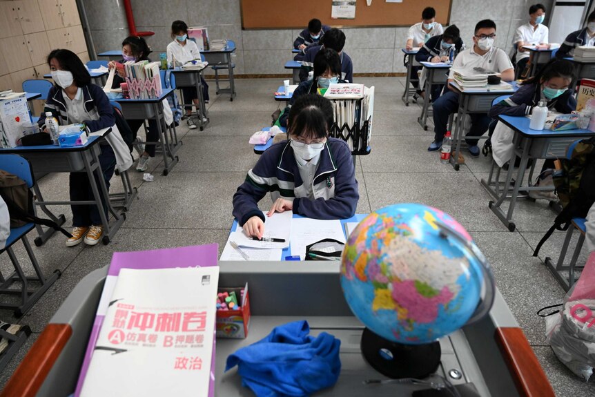 School-aged students wearing face masks sit at desks spaced out across a classroom.