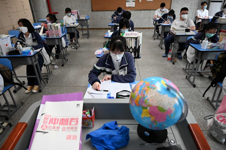 School-aged students wearing face masks sit at desks spaced out across a classroom.