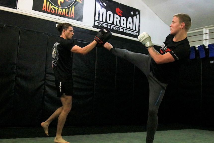 Two men in dark clothing sparring in a gym.