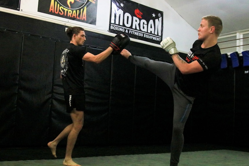 Two men in dark clothes sparring in the gym.