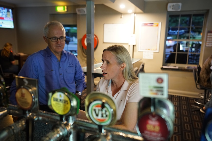 A man and woman stand at a bar in a pub.
