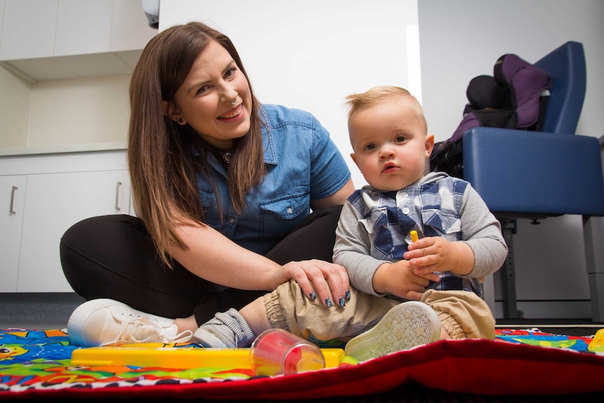 Brie Davis and Max sit on a colourful play mat.