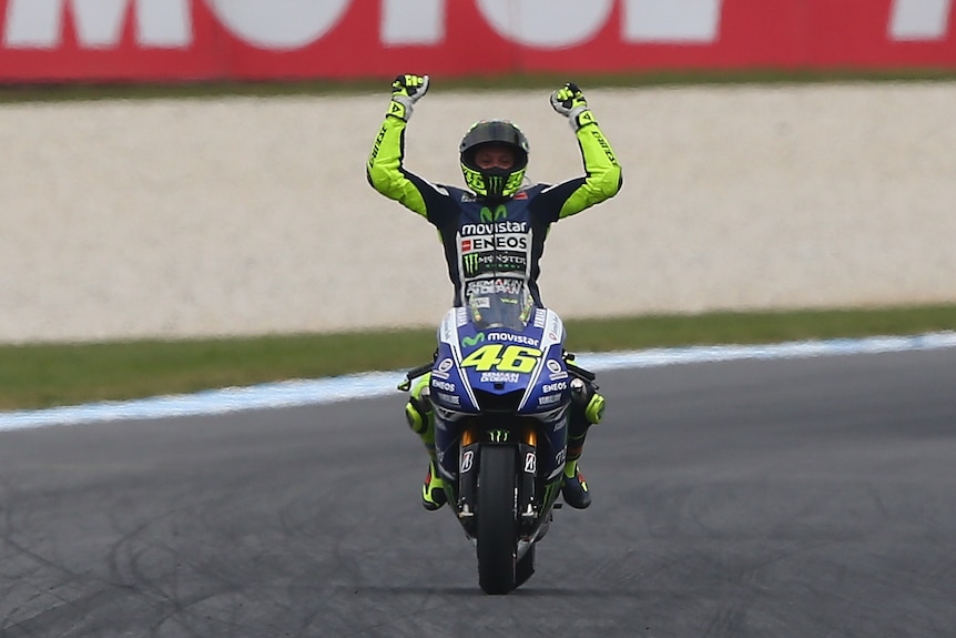 Italian motorcyclist Valentino Rossi raises his arms in triumph as he coasts on his bike after winning a MotoGP race.