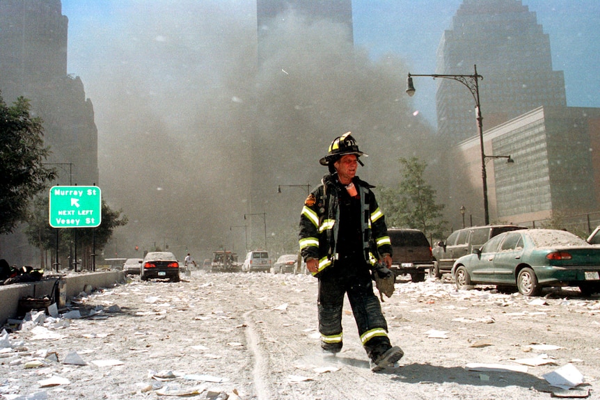 A New York City firefighters walks down a road surrounded by brown smog 