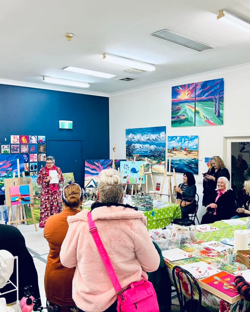a group of women sitting in a bright room looking at a woman talk to the class
