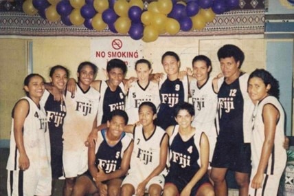 A group of young women, all wearing black and white basketball singlets saying 'Fiji', have their arms around each other