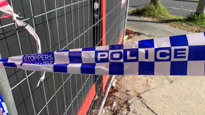 A strip of police tape with a fence and concrete footpath in the background.