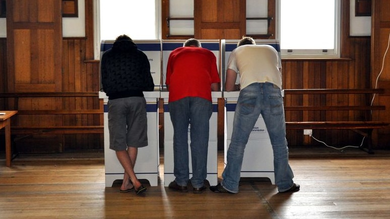 Three people cast votes in a hall.
