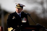 Vice Admiral Mark Hammond stands behind a microphone in full uniform wearing medals.