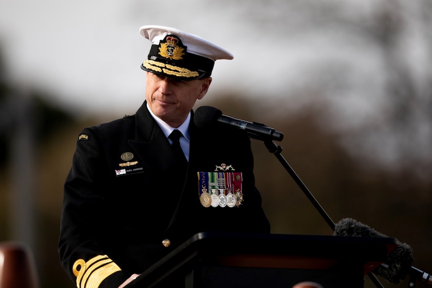 Il vice ammiraglio Mark Hammond in piedi dietro un microfono in uniforme e con indosso medaglie.