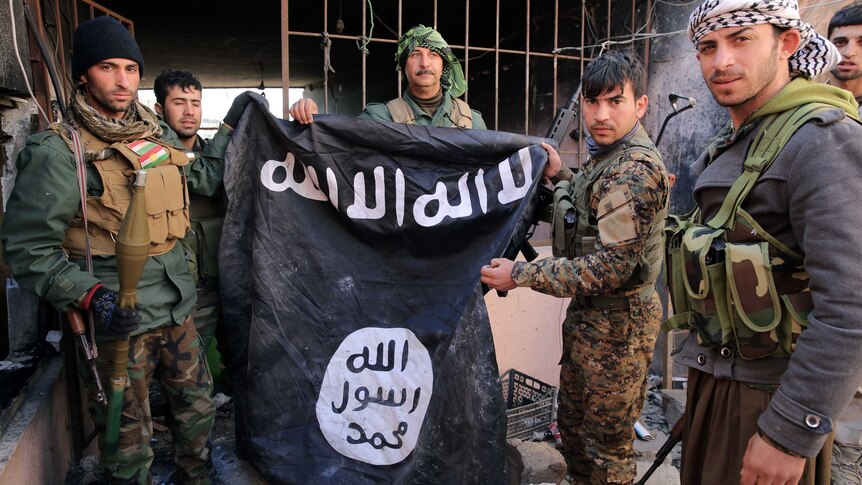 Kurdish and Yazidi forces hold an Islamic State flag after retaking the Yazidi town of Sinjar