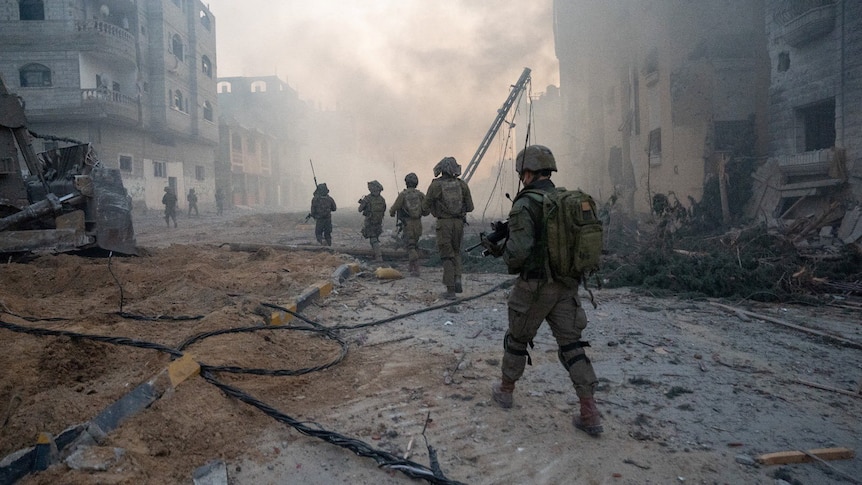 A group of soldiers walk through a wrecked, dusty street.