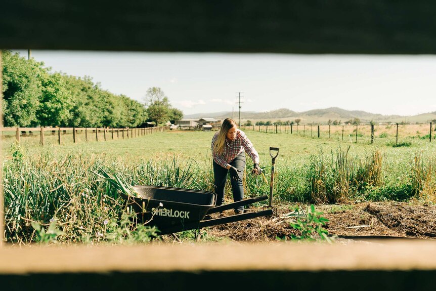 Young blonde woman doing gardening in a paddock on a farm property.