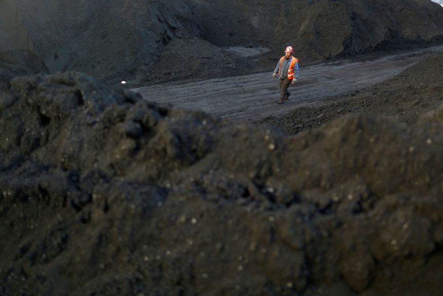 A worker walks past coal piles at a coal coking plant in Yuncheng, Shanxi province, China