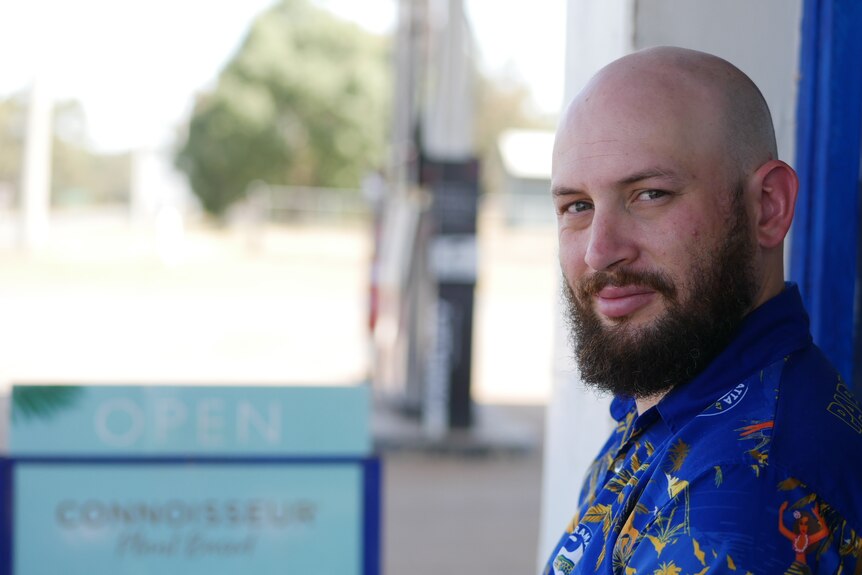 A bald, beaded man stares into the camera with a blurred servo pump in the background.