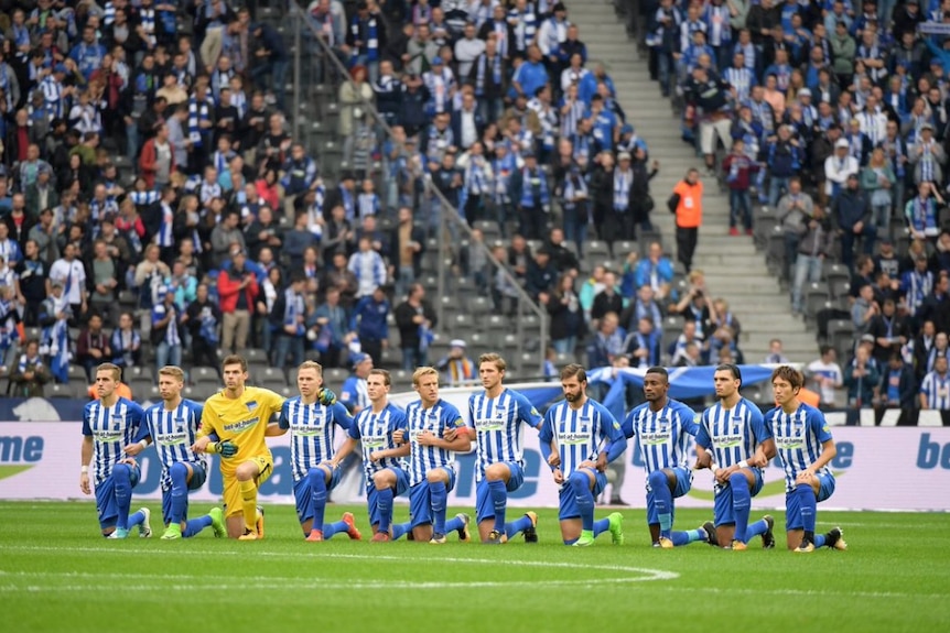 Hertha Berlin players kneel during the German national anthem.