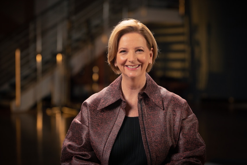 A professional photo of Julia Gillard, who looks straight at the camera, wearing a maroon jacket, the background is out of focus