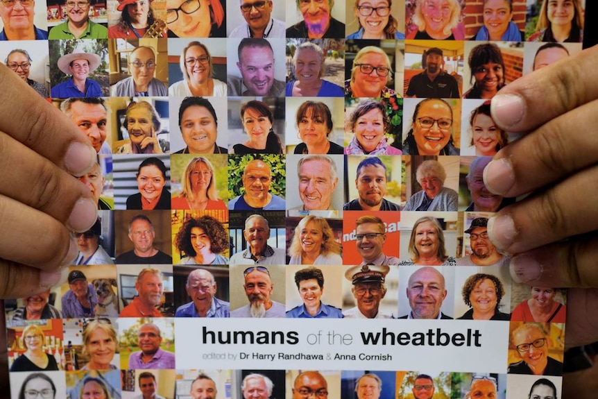 The hands of an Aboriginal man holding a book featuring many people's faces, called Humans of the Wheatbelt.