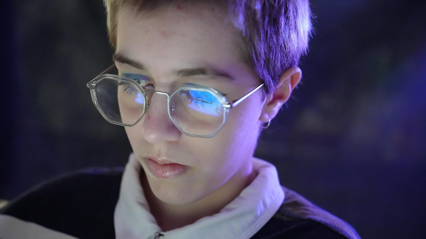 Boy wearing glasses with phone light reflecting on his lenses 