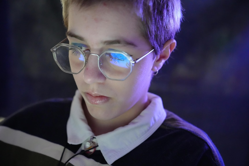 Boy wearing glasses with phone light reflecting on his lenses 