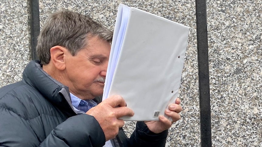 A man attempts to cover his face with a book binder.