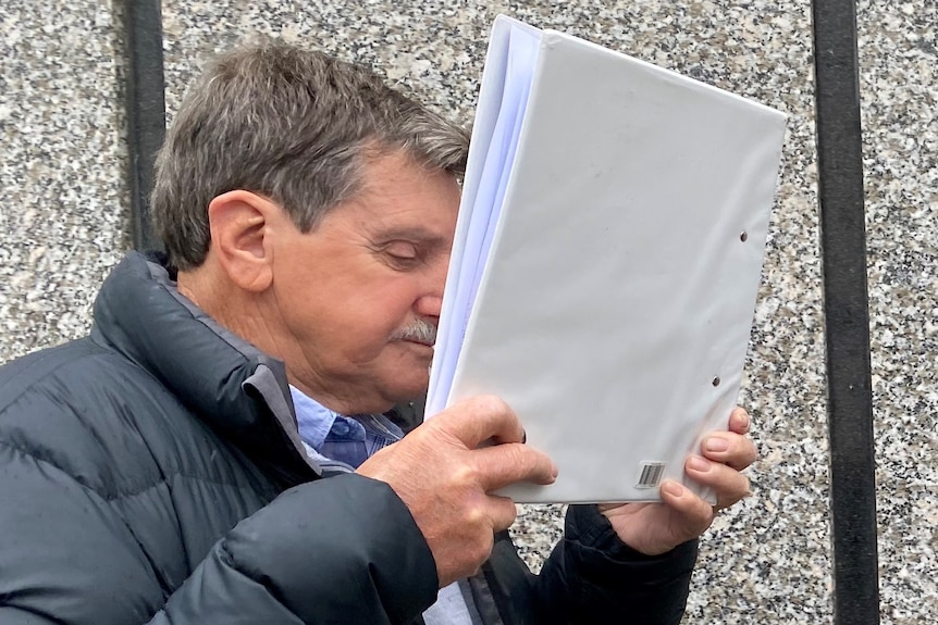 A man attempts to cover his face with a book binder.