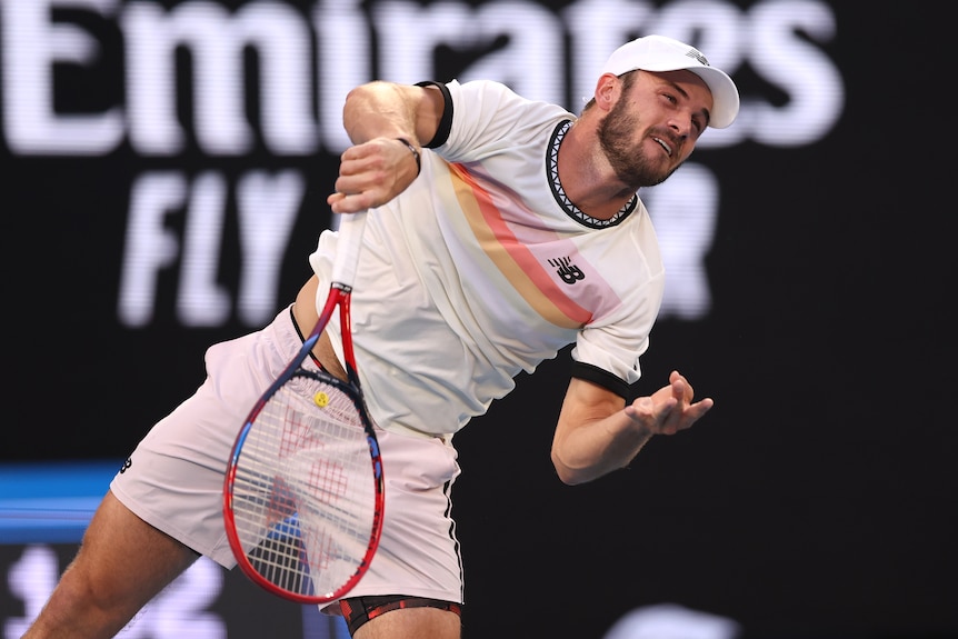 Un joueur de tennis masculin américain sert lors d'un match contre Novak Djokovic.