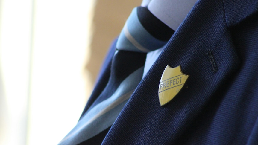 Close up of a school uniform with blazer, tie and prefect badge.