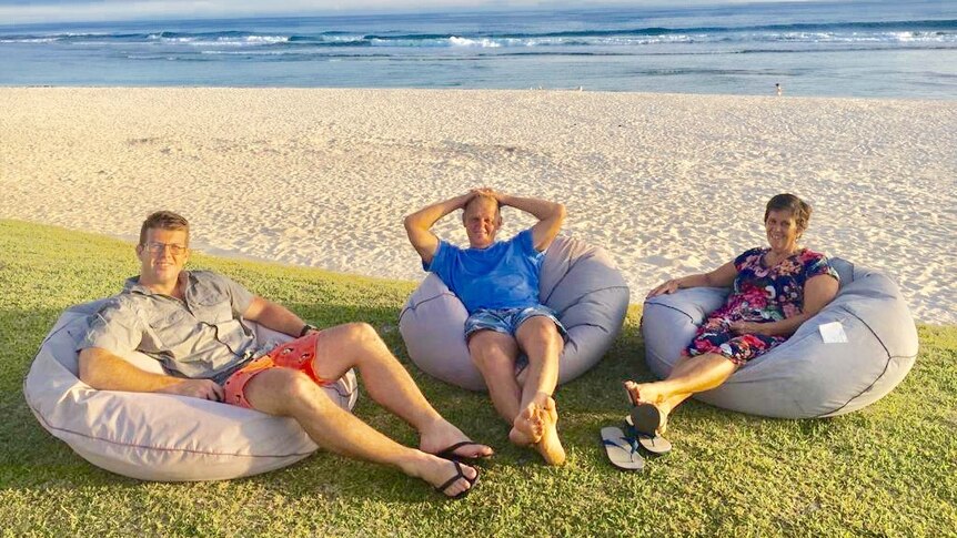 Yaric Robinson (left) with his father and mother on beanbags on a beach in Vanuatu.