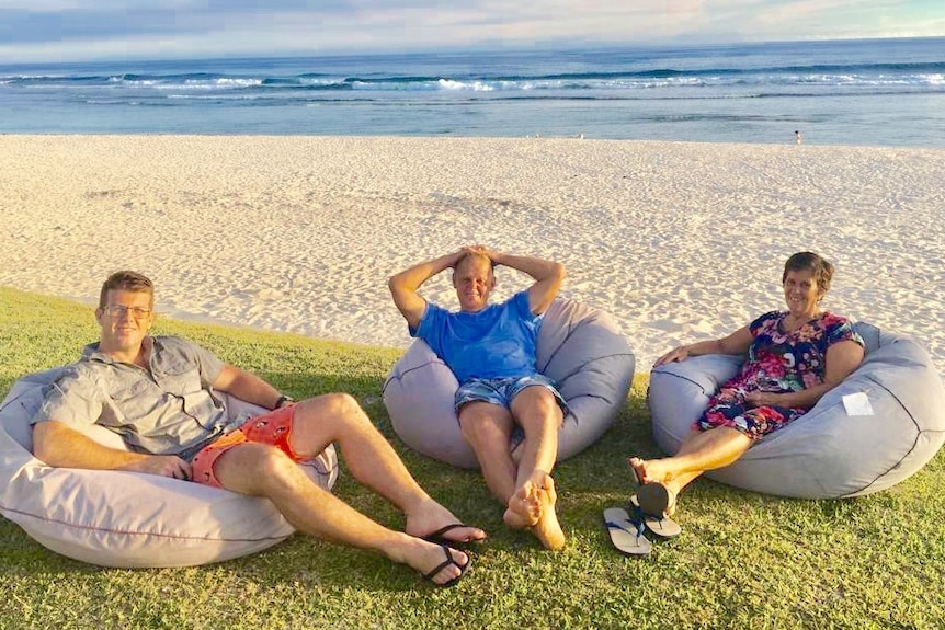 Yaric Robinson (left) with his father and mother on beanbags on a beach in Vanuatu.