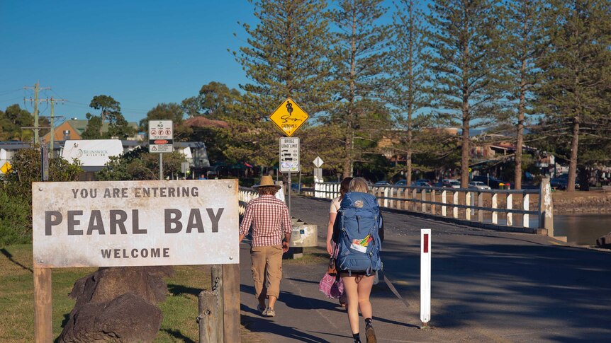 People walk past a sign reading 'you are entering Pearl Bay welcome'