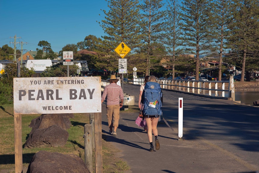 People walk past a sign reading 'you are entering Pearl Bay welcome'
