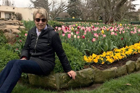 A woman sits on a rock wall next to a garden of tulips.