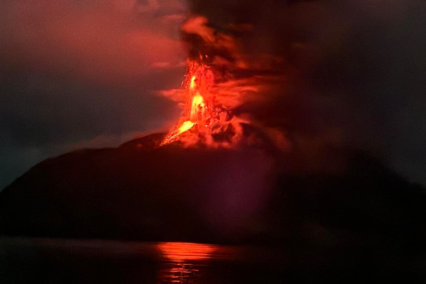 Bright red lava and ash erupts into the sky from a dark mountain